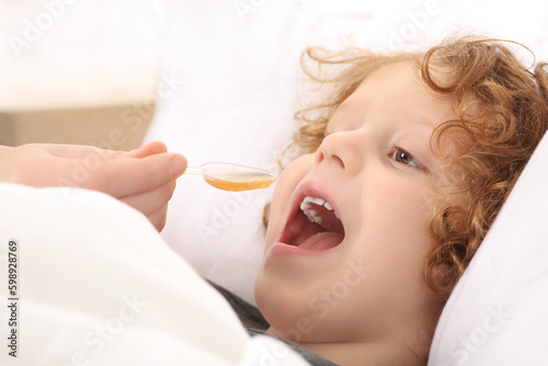 Mother giving cough syrup to her son on bed, closeup