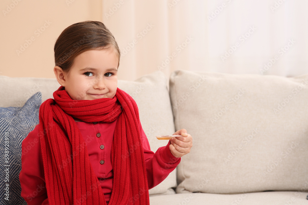 Cute girl holding measuring spoon with cough syrup on sofa indoors, space for text. Effective medicine Cute girl holding measuring spoon with cough syrup on sofa indoors, space for text. Effective medicine