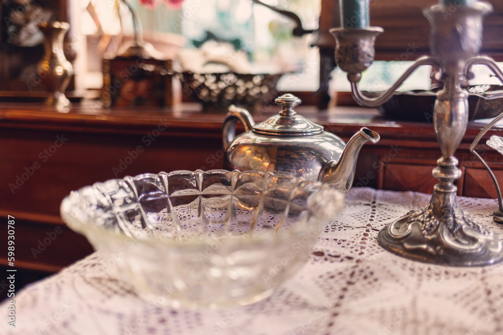 Vintage furniture and glassware on table with napkin. Silver teapot and candlestick. Retro interior of coffee shop