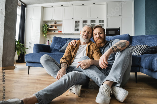 Smiling gay men looking at camera while sitting on floor at home. 