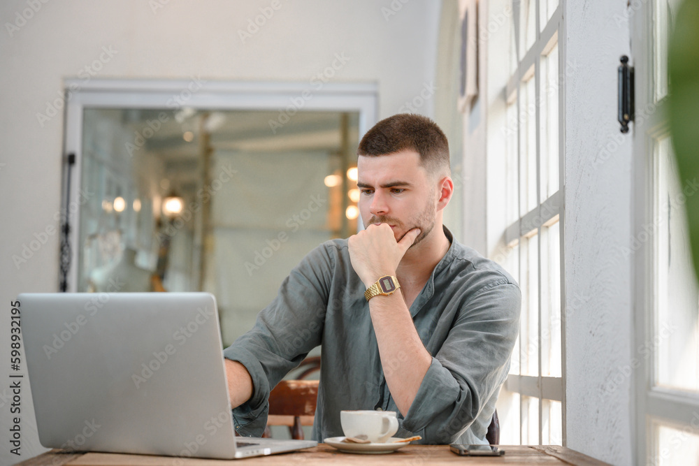 young freelancer working online at coffee shop using laptop computer handsome young man freelancer sit and work outside the workplace