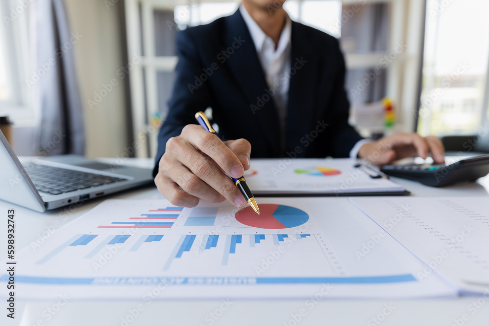 A business man working on a laptop comparing details from graphs Business income chart in real estate, tax, management, marketing, technology in private office. A business man working on a laptop comparing details from graphs Business income chart in real estate, tax, management, marketing, technology in private office.