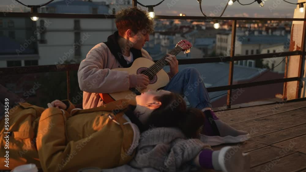 4k Lesbian couple plays guitar while on rooftop date spbd. Young beautiful women playing musical instrument and looking with smiles, posing and sitting on roof during evening sunset. Happy homosexual 4k Lesbian couple plays guitar while on rooftop date spbd. Young beautiful women playing musical instrument and looking with smiles, posing and sitting on roof during evening sunset. Happy homosexual