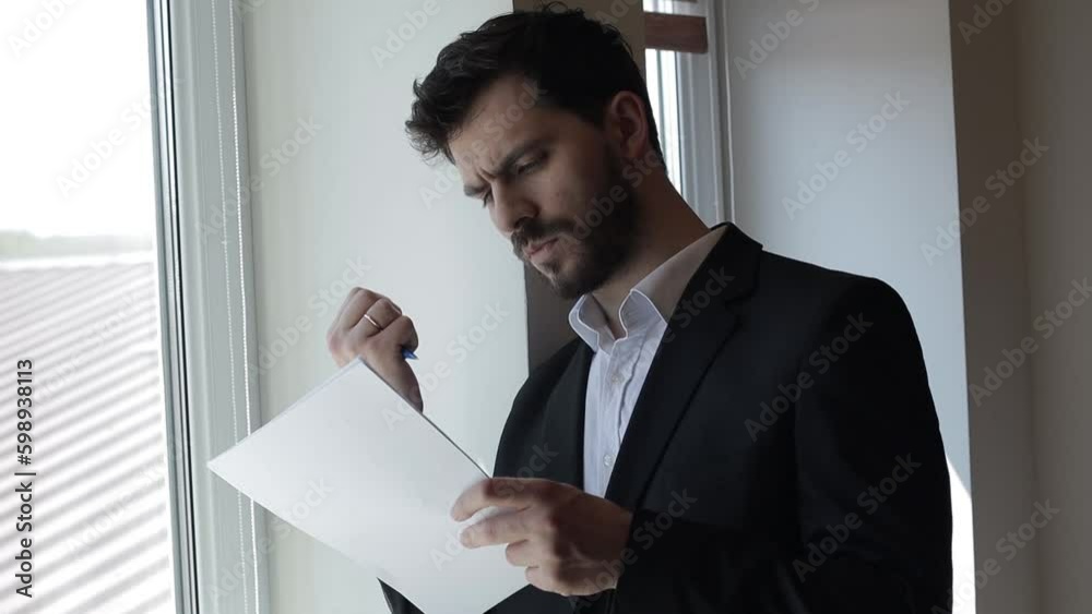 Bearded Middle Aged Businessman in a Suit Writing in a Notebook Indoors Near a Window