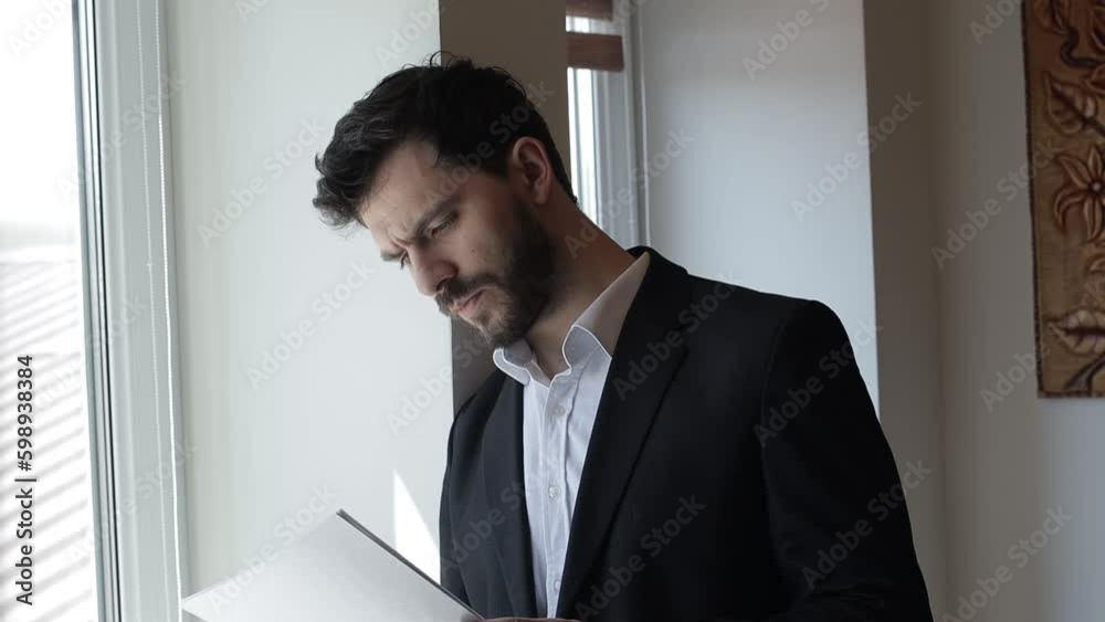 Bearded Middle Aged Businessman in a Suit Writing in a Notebook Indoors Near a Window Bearded Middle Aged Businessman in a Suit Writing in a Notebook Indoors Near a Window