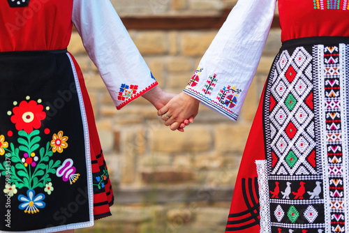 Girls in traditional bulgarian ethnic costumes with folklore embroidery holding hands. The spirit of Bulgaria - culture, history and traditions.