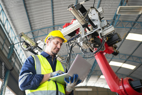 Male technician programs a robot arm with a digital tablet and assembly robot in a factory. Apprentice engineers programming robots in factory.