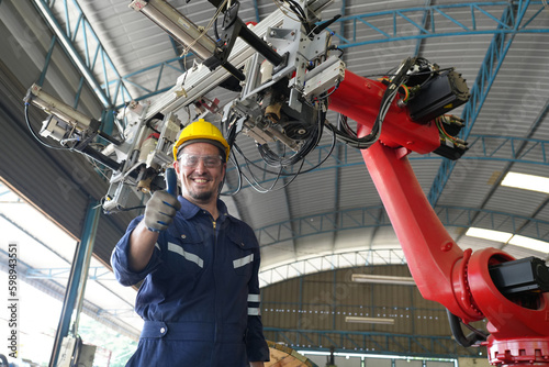 Male technician programs a robot arm with a digital tablet and assembly robot in a factory. Apprentice engineers programming robots in factory.