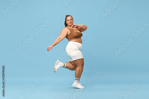 Fototapeta Naklejka Na Ścianę i Meble -  Active lifestyle and loss of calories. Young overweight woman training in sportswear against blue studio background. Concept of sport, body-positivity, weight loss, body and health care