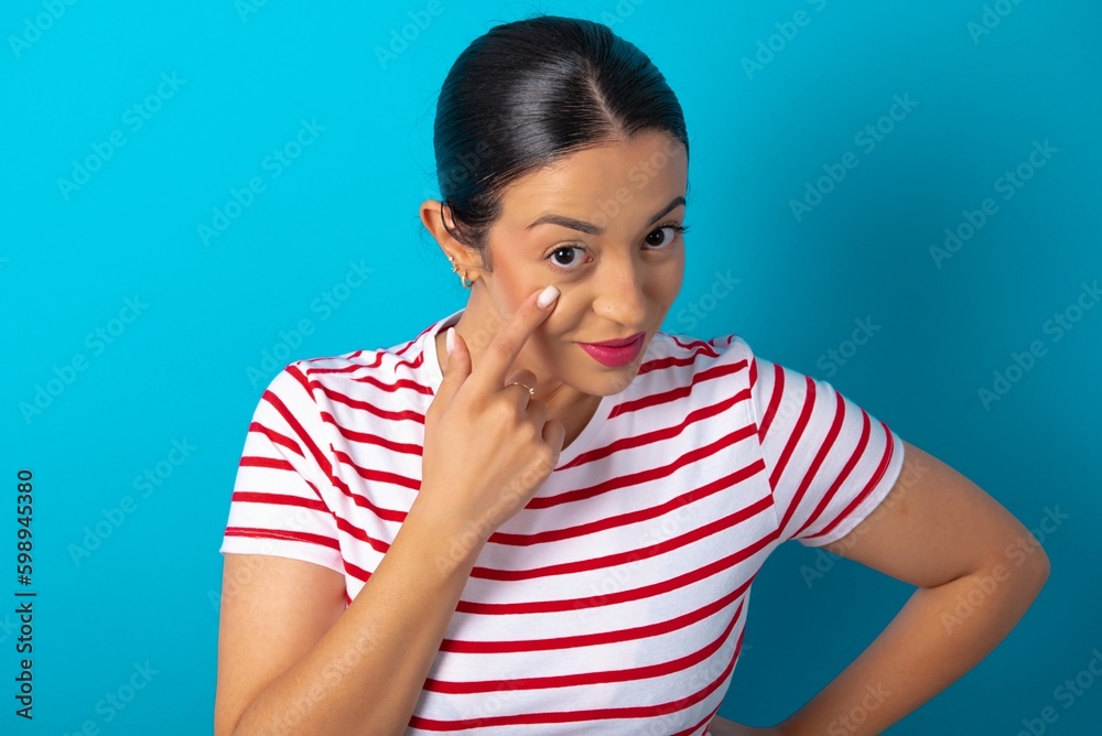 beautiful woman wearing striped T-shirt over blue studio background , looking, observing, keeping an eye on an object in front, or watching out for something. beautiful woman wearing striped T-shirt over blue studio background , looking, observing, keeping an eye on an object in front, or watching out for something.