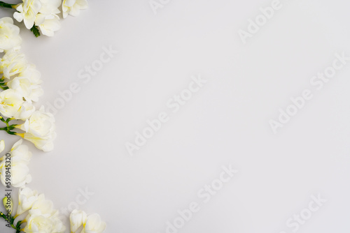 Spring blossom frame. White flowers on light grey background. Summer holiday composition. Fresh freesia template for product advertising or sale. Top view, flat lay, copy space. Blooming layout.