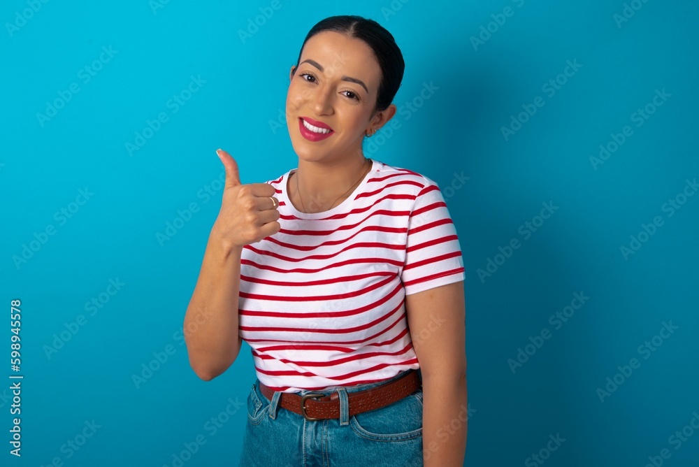 beautiful woman wearing striped T-shirt over blue studio background giving thumb up gesture, good Job! Positive human emotion facial expression body language. beautiful woman wearing striped T-shirt over blue studio background giving thumb up gesture, good Job! Positive human emotion facial expression body language.