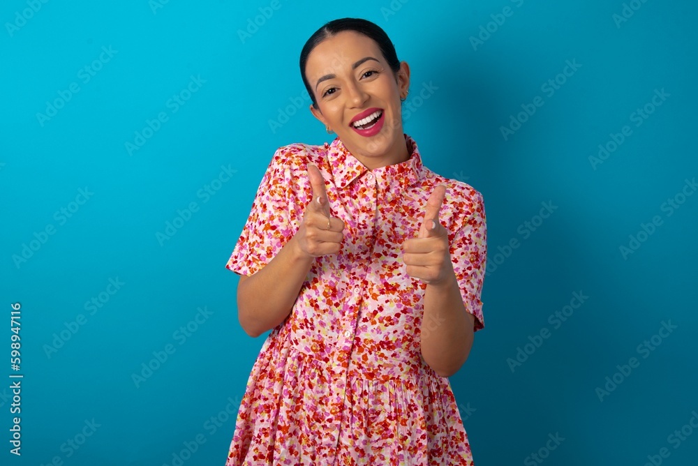 beautiful woman wearing floral dress over blue studio background directs fingers at camera selects someone. I recommend you. Best choice beautiful woman wearing floral dress over blue studio background directs fingers at camera selects someone. I recommend you. Best choice