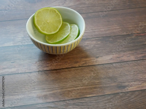 Slices of lime fruit in a bowl on a wooden table 