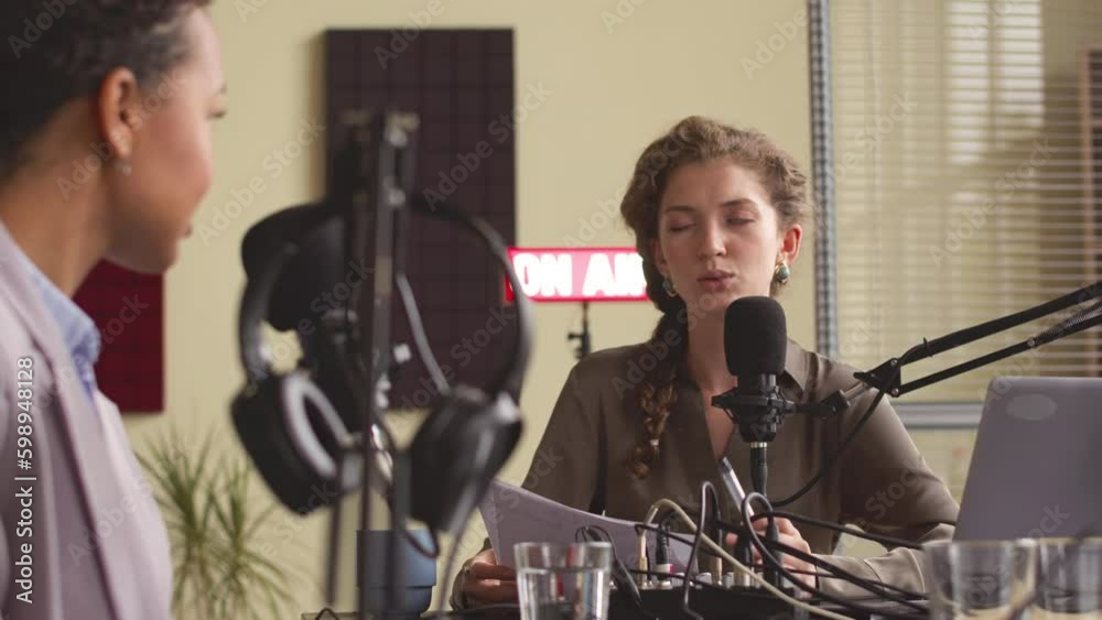 Waist up of young Caucasian female radio host asking businesswoman questions while broadcasting live in studio Waist up of young Caucasian female radio host asking businesswoman questions while broadcasting live in studio