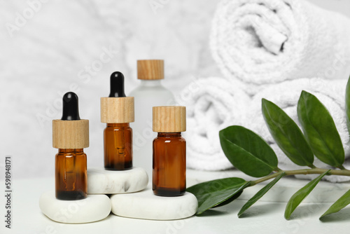 Bottles of essential oil, green leaves and spa stones on white table