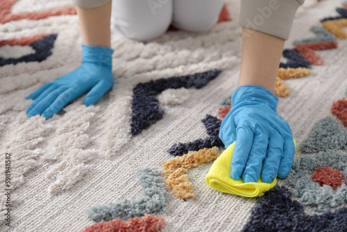 Woman in rubber gloves cleaning carpet with rag indoors, closeup © New Africa