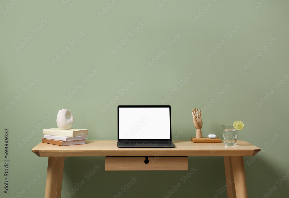Stylish workplace with laptop, books and decor on table near light green wall Stylish workplace with laptop, books and decor on table near light green wall