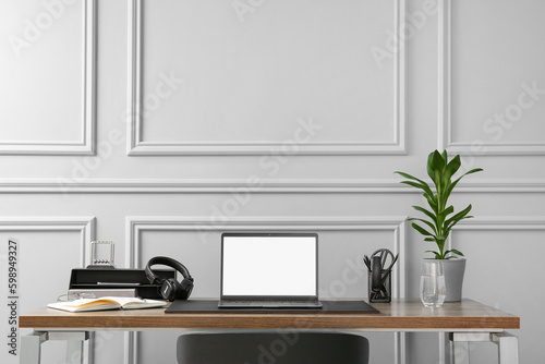 Stylish workplace with laptop, houseplant and stationery on wooden table near light grey wall