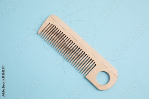 Wooden comb with lost hair on light blue background, top view