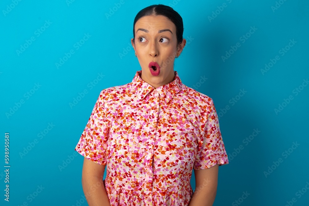 Φωτογραφία Shocked beautiful woman wearing floral dress over blue studio background look empty space with open mouth screaming: Oh My God! I can't believe this