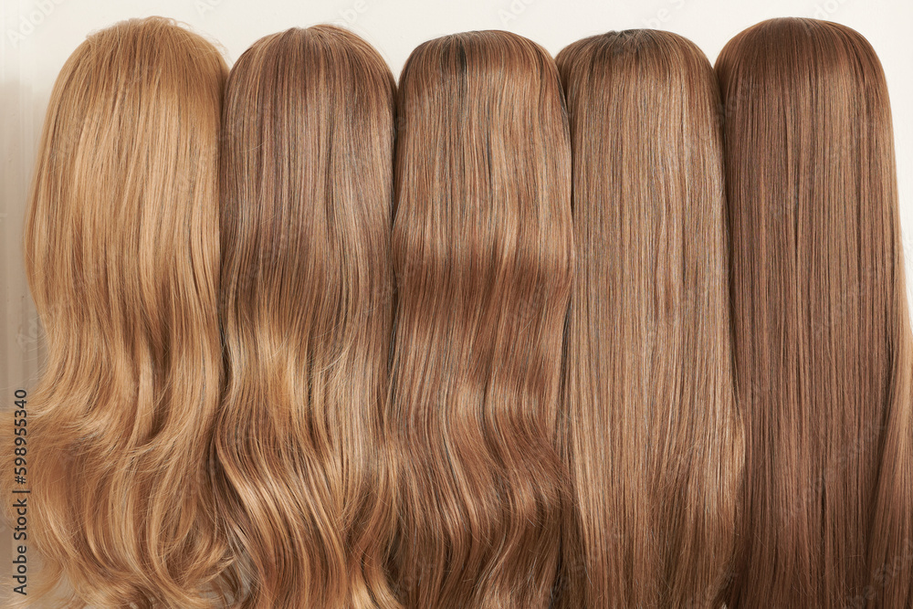 Showcase of natural looking wigs in different shades of blonde fixed on the wig holders in beauty salon. Row of mannequin heads with variation colors fair hair on shelf in wig shop Showcase of natural looking wigs in different shades of blonde fixed on the wig holders in beauty salon. Row of mannequin heads with variation colors fair hair on shelf in wig shop