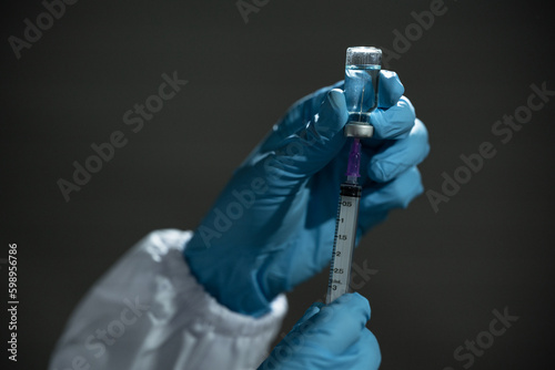 Doctor hand in blue gloves holding influenza vaccine for prevention human.Concept fight against human papilloma virus, nurse in laboratory holding a syringe with HPV vaccines for girl and woman. photo