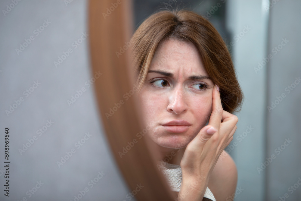 Young beautiful woman looking at mirror and confusing because of new wrinkles Young beautiful woman looking at mirror and confusing because of new wrinkles