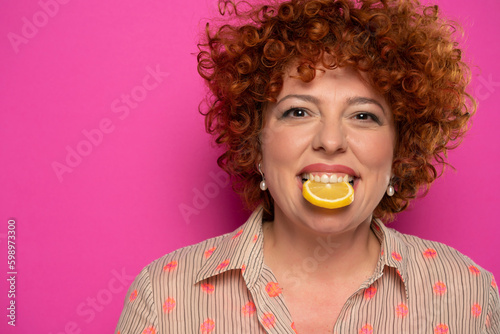Portrait of a curly redhead woman with lemon slice in her mouth, cut out.