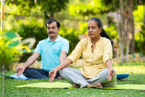 Indian senior couple doing meditation or yoga at park - concept of healthy lifestyle, mental wellness and self acre. photo