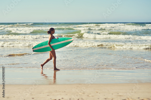 Its time to hit the waves. a young woman out at the beach with her surfboard.