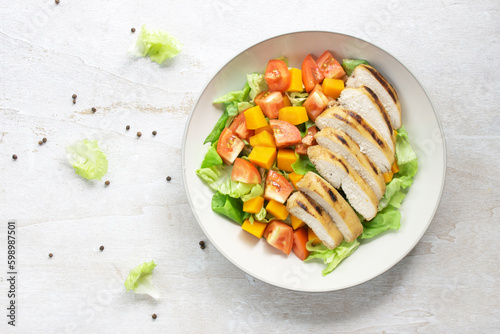 Healthy food grilled chicken vegetable pumpkin lettuce tomato salad in bowl on white wood table.