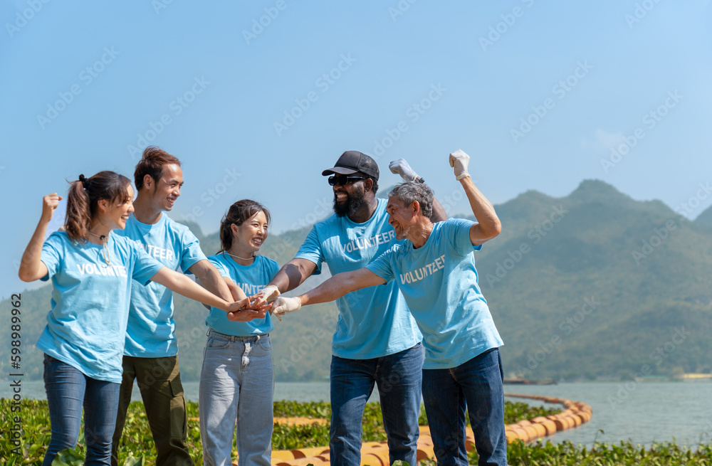 Group of happy multi-ethnic diverse volunteers joining hands stack together and raising hands with smile to show the power of unity in charity work, key to success in making future a better world