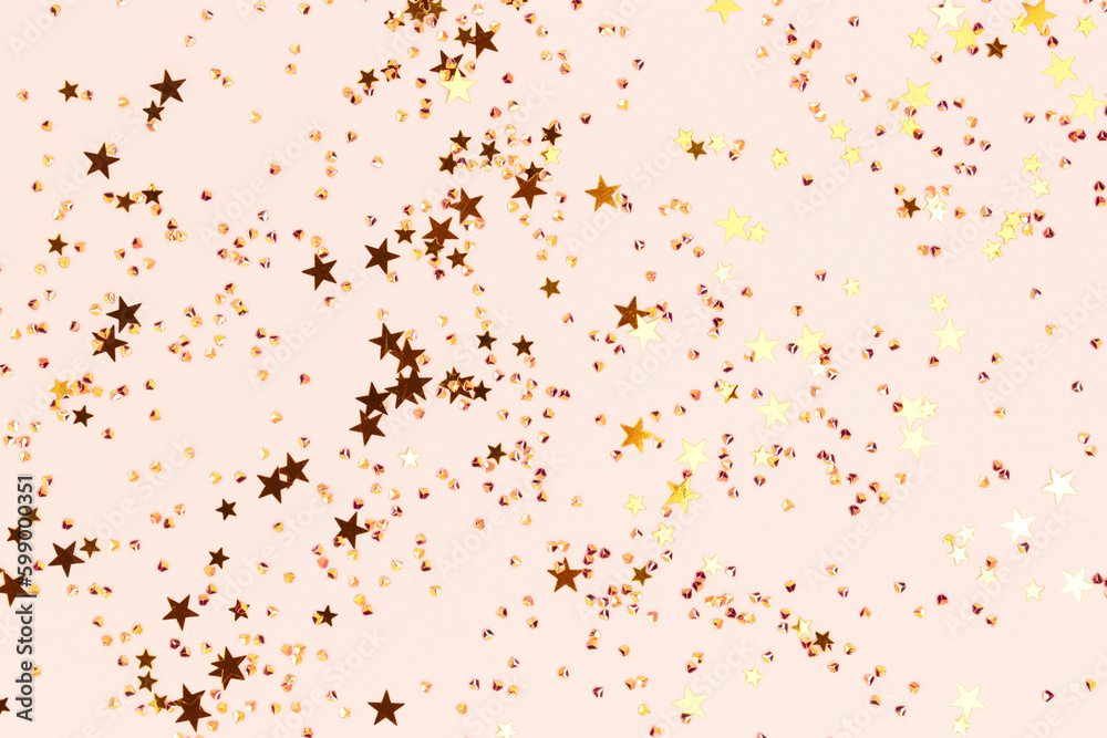 Shiny gold colored stars and crystals confetti on a beige background. Festive texture. Selective focus.
