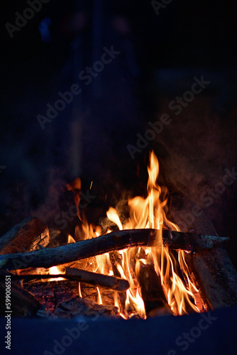 Close-up of a campfire. Fire burning brightly with a big yellow and orange flame in the dark. Firewood and logs burning to ember and ash. Enjoying the warmth of the fire at a cold winter night.
