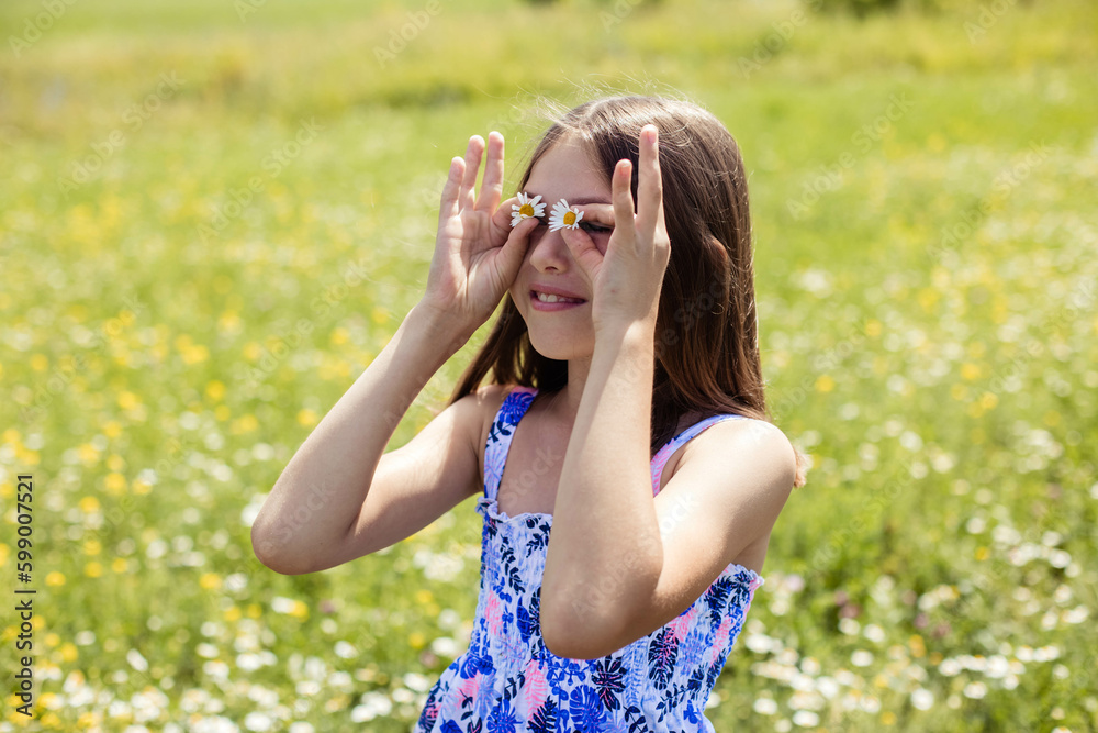Close-up portrait of a pretty girl in a field, smiling and covering her face with flowers with daisies, looks away