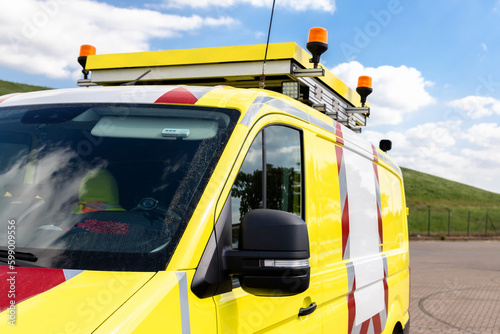 Yellow special cargo escort road traffic car roof mounted digital sign board. Repair and service van with ladder and orange light bar on roof at city street. Assistance or installation team vehicle