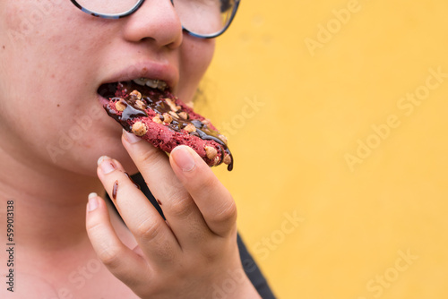 Girl bitting a red chocolate cookies with chocolate sauce