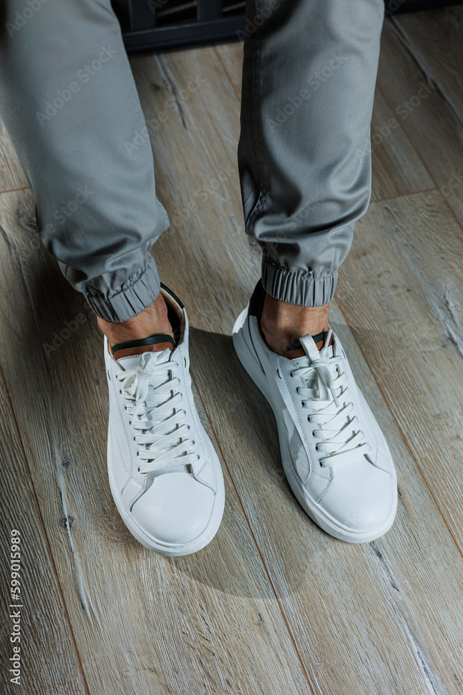 Men's summer shoes. Close-up of male legs in white leather sneakers. Collection of men's leather shoes