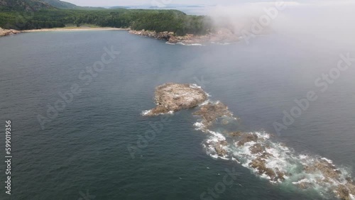 4K Aerial Drone orbit arc through clouds around small rocky island with waves crashing. Trees, Mountains, Water, Coast visible