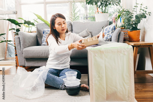 Asian female separate garbage at home. young woman sorting and recycling plastic, paper, aluminum can and food container to trash bins in living room at apartment. recycling and sustainability at home