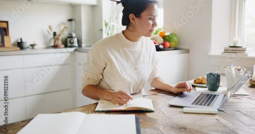 Young woman drawing in a sketchbook and working on a laptop while sitting at a table in her kitchen at home
