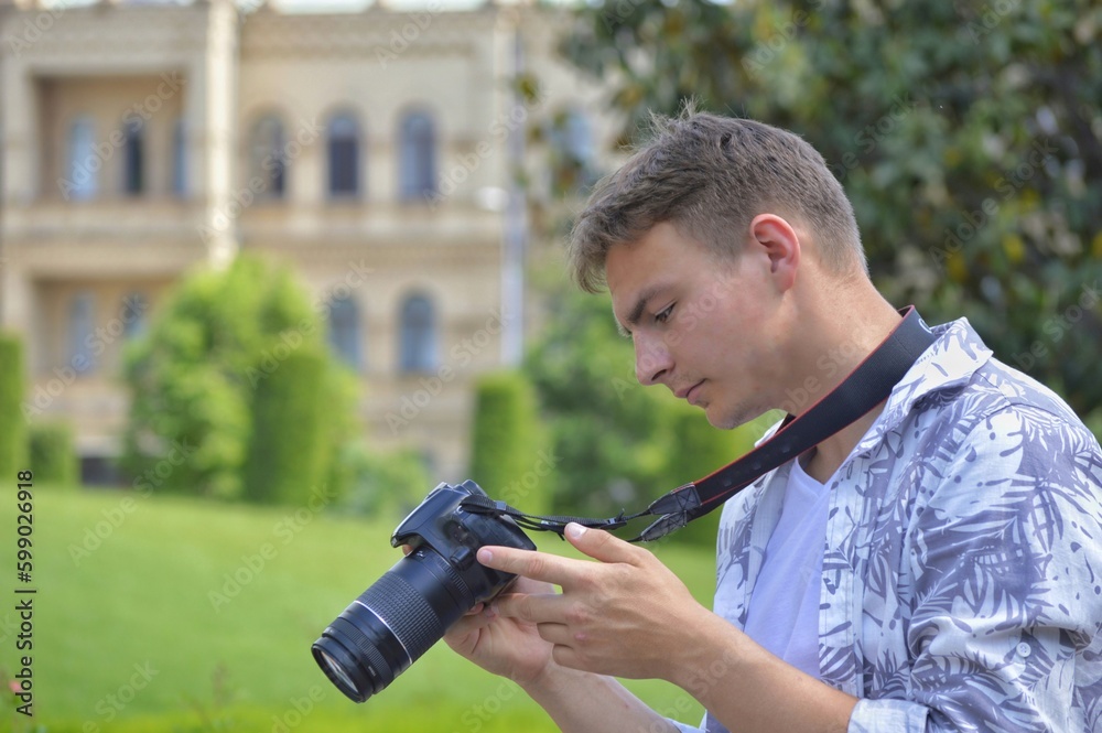 A young European-looking photographer in a white shirt with a camera around his neck looks into camera display