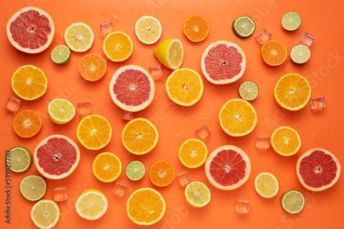 Fresh sliced and halved citrus fruits spread with clear ice cubes and water drops on orange background.