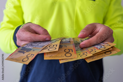 Fotografie View of a tradesman in high visibility clothes holding australian dollar notes