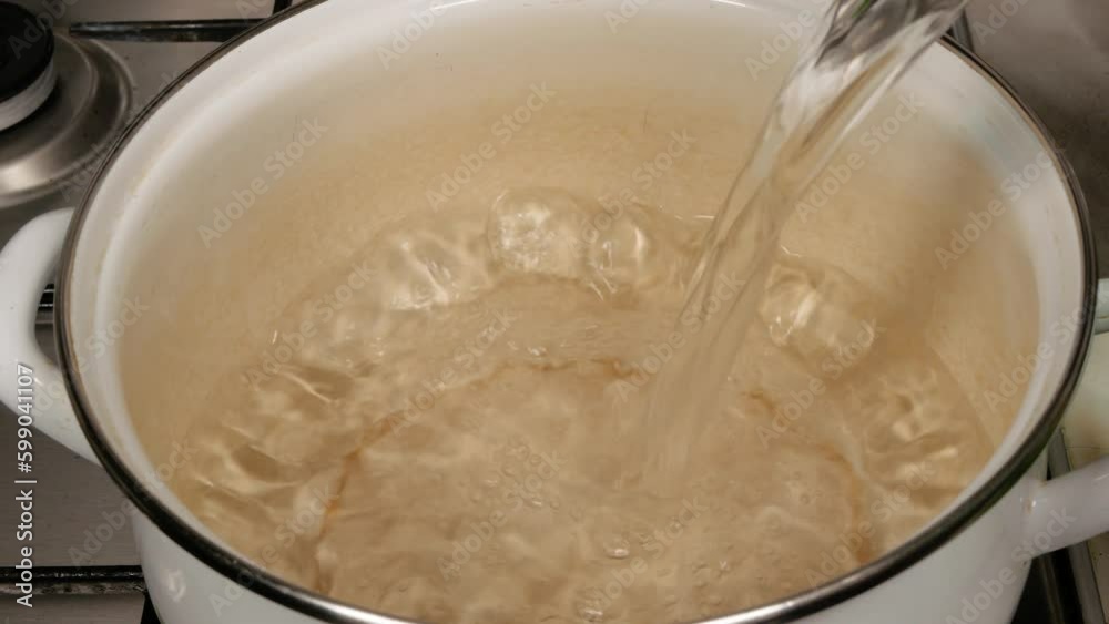 The cook pours water into a white pan, close-up, top view. The cook pours water into a white pan, close-up, top view.