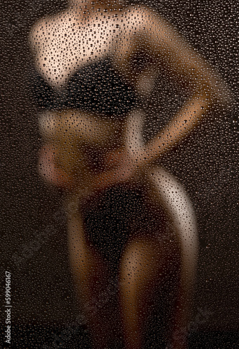 Slender woman in black underwear in the shower on a dark background.