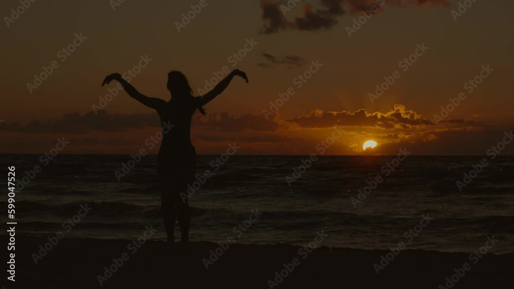 static wide shot of a woman in silhouette dancing by the sea against the background of the setting sun, 4k, slow motion static wide shot of a woman in silhouette dancing by the sea against the background of the setting sun, 4k, slow motion