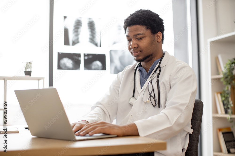 Attractive african american male in lab coat working on laptop