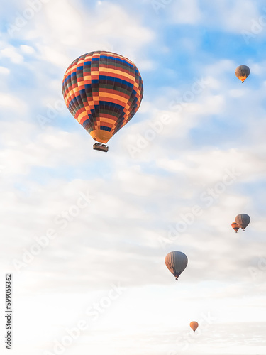 Flying in sky many bright colored beautiful balloons into air in Cappadocia in mountains early at sunrise, dawn. Filling balloon with hot air from burner, big basket. Tourists excursion, cloud flight